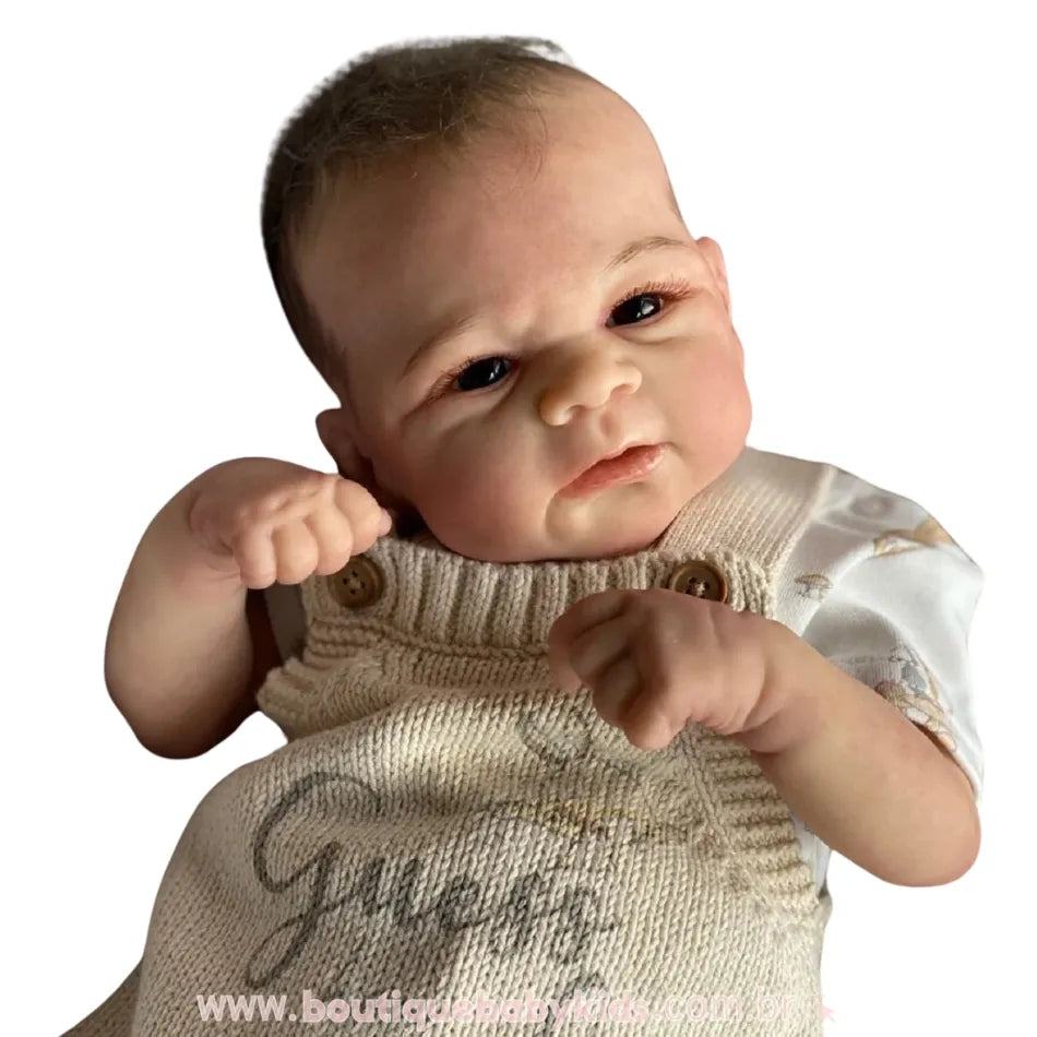 Close da Boneca Bebê Reborn Realista Bryan com jardineira bege e fundo branco.