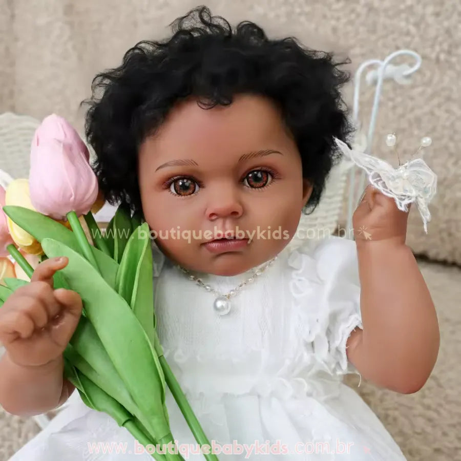 Close-up do rosto da Boneca Bebê Reborn Cecília negra com cabelos cacheados, mostrando detalhes realistas da pele, olhos castanhos brilhantes, cabelos cacheados pretos e colar de pérolas delicado.