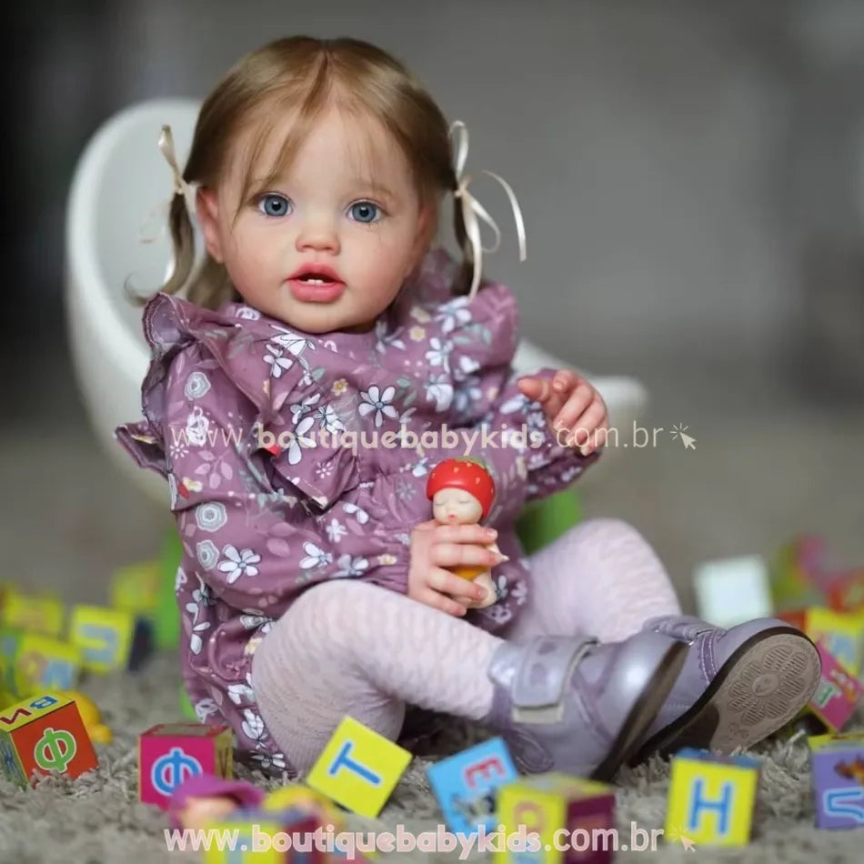 Boneca Bebê Reborn Julia com vestido lilás de flores e laços no cabelo, sentada entre blocos coloridos e segurando brinquedo.