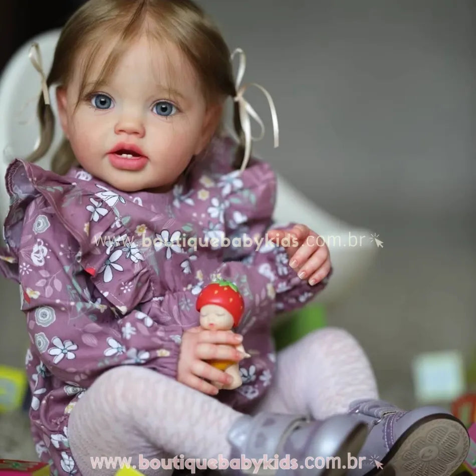 Boneca Bebê Reborn Julia com expressão realista, segurando boneco com chapéu de morango, vestida com roupa floral roxa.