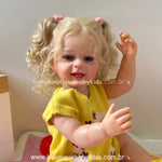 Close lateral da boneca Lara com cabelos cacheados loiros e presilhas rosas, sorrindo.