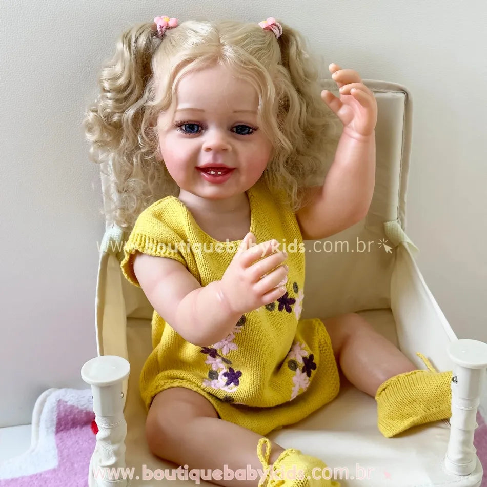 Boneca Lara sentada em cadeirinha branca, com vestido amarelo de tricot bordado com flores.