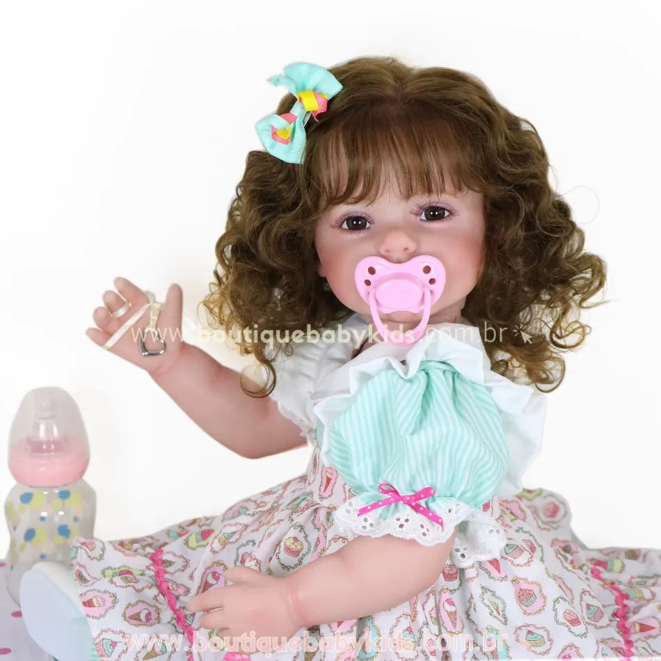 Boneca Bebê Reborn Maria sentada com vestido colorido, laço no cabelo e chupeta rosa na boca.