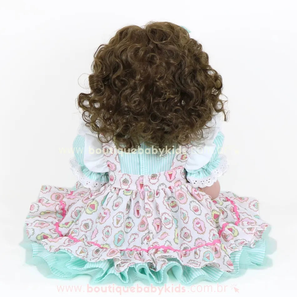 Vista traseira da Boneca Bebê Reborn Maria destacando o volume dos cabelos cacheados e vestido com babados.