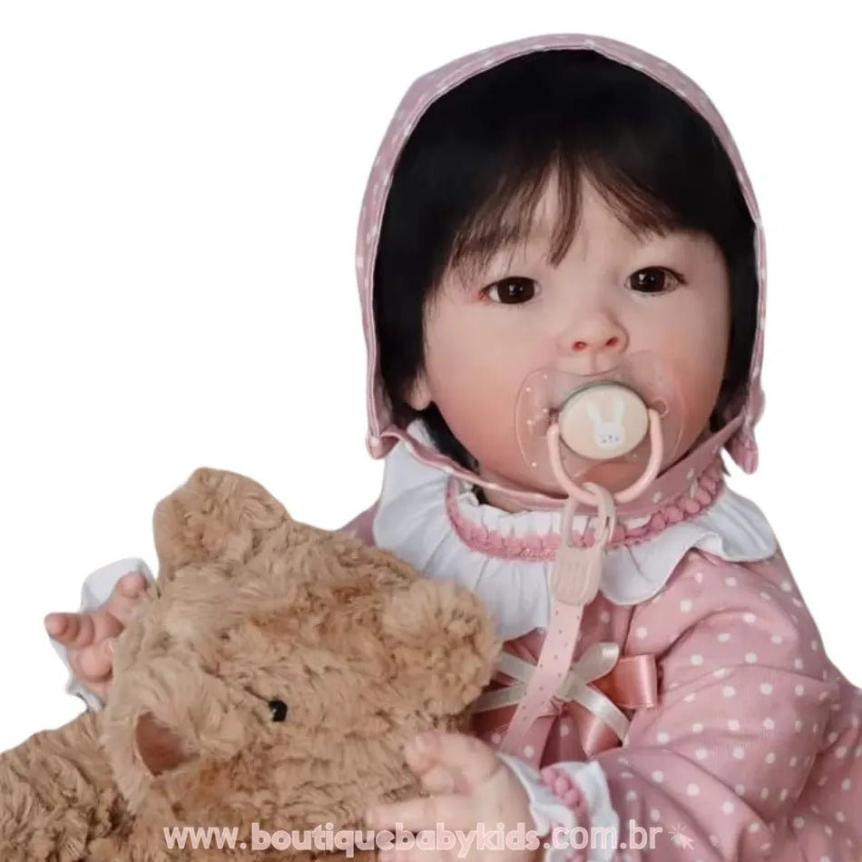 Close da boneca bebê reborn asiática com touca rosa de poá e chupeta com magnética desenho de coelhinho, abraçando um ursinho fofo.