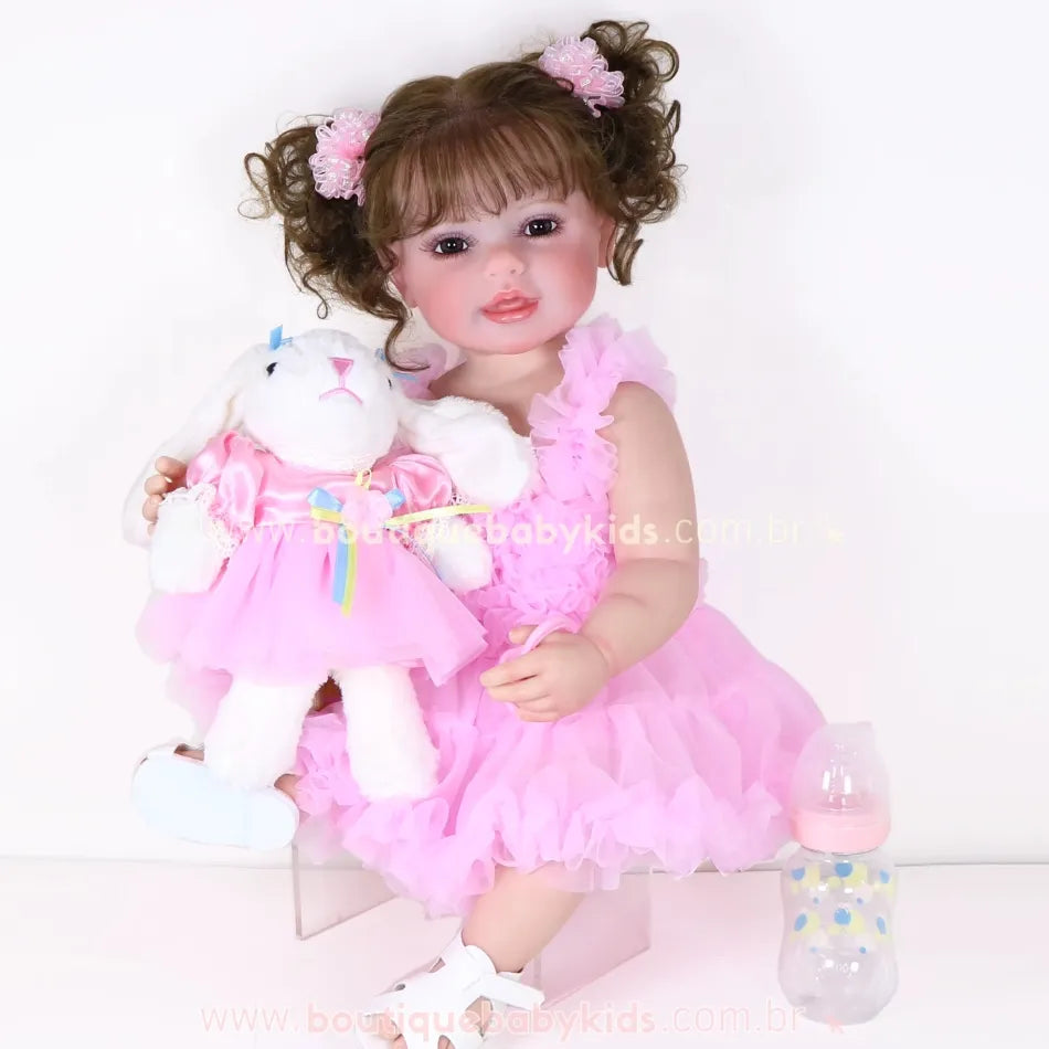 Boneca Bebê Reborn Rebecca sentada com coelhinha de pelúcia no colo, vestindo vestido rosa com babados e cabelo preso com lacinhos rosa