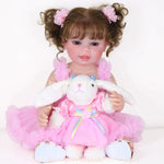 Boneca Reborn Rebecca com vestido rosa e coelha de pelúcia no colo, sorrindo para a câmera