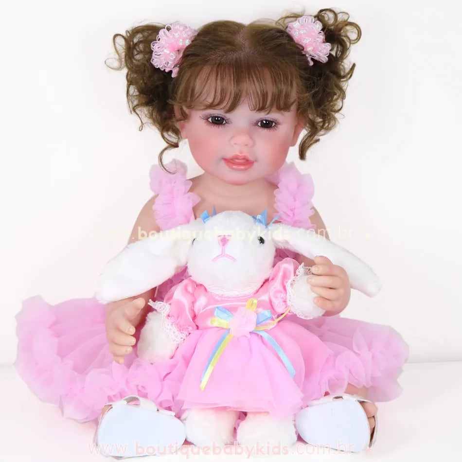 Boneca Reborn Rebecca com vestido rosa e coelha de pelúcia no colo, sorrindo para a câmera