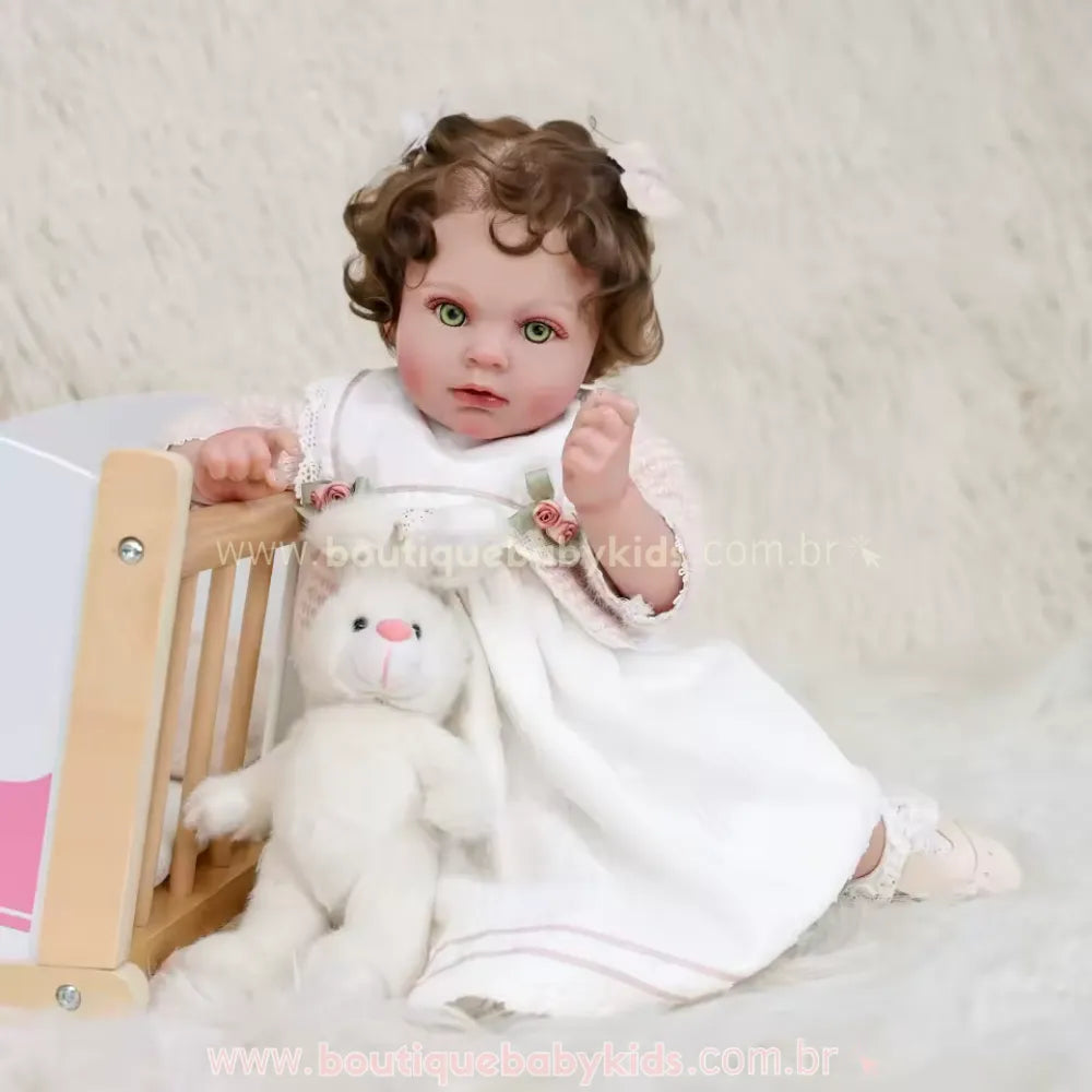 Boneca Bebê Reborn Stella sentada no chão sobre tapete felpudo, encostada em um berço de madeira de brinquedo, com um coelho de pelúcia branco no colo.