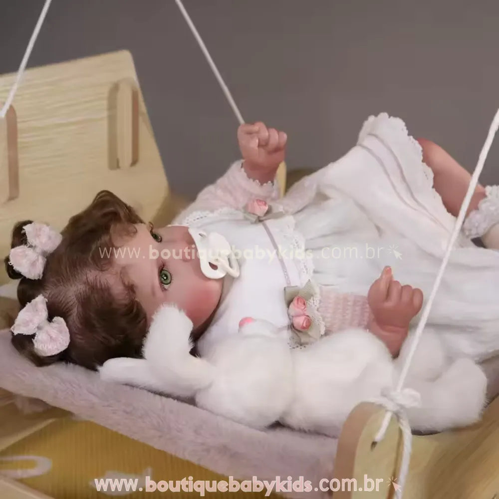 Boneca Bebê Reborn deitada em berço de balanço de madeira, usando chupeta magnética, vestido branco e bolero de tricô rosa, com coelho de pelúcia ao lado.