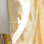 Close-up da barra da capa infantil dourada, destacando o brilho do tecido aveludado e o acabamento em pelúcia. 