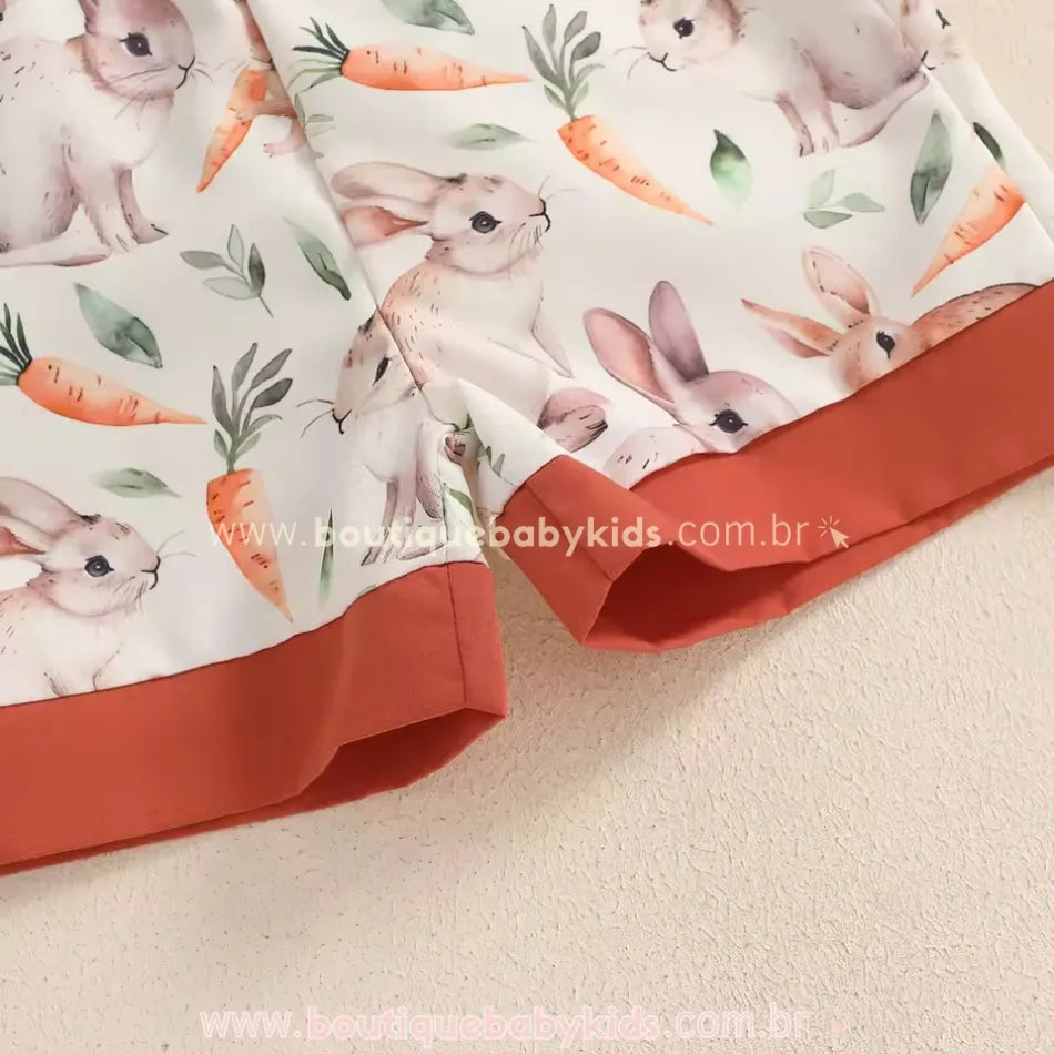 Close-up do short infantil com estampa temática de coelhos e cenouras, barra contrastante em tom terroso e tecido macio. Modelo confortável para bebês, ideal para a Páscoa.