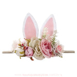 Faixa decorada com flores românticas em tons pastéis e orelhinhas de coelho em tecido branco e rosa, um acessório perfeito para ocasiões festivas.