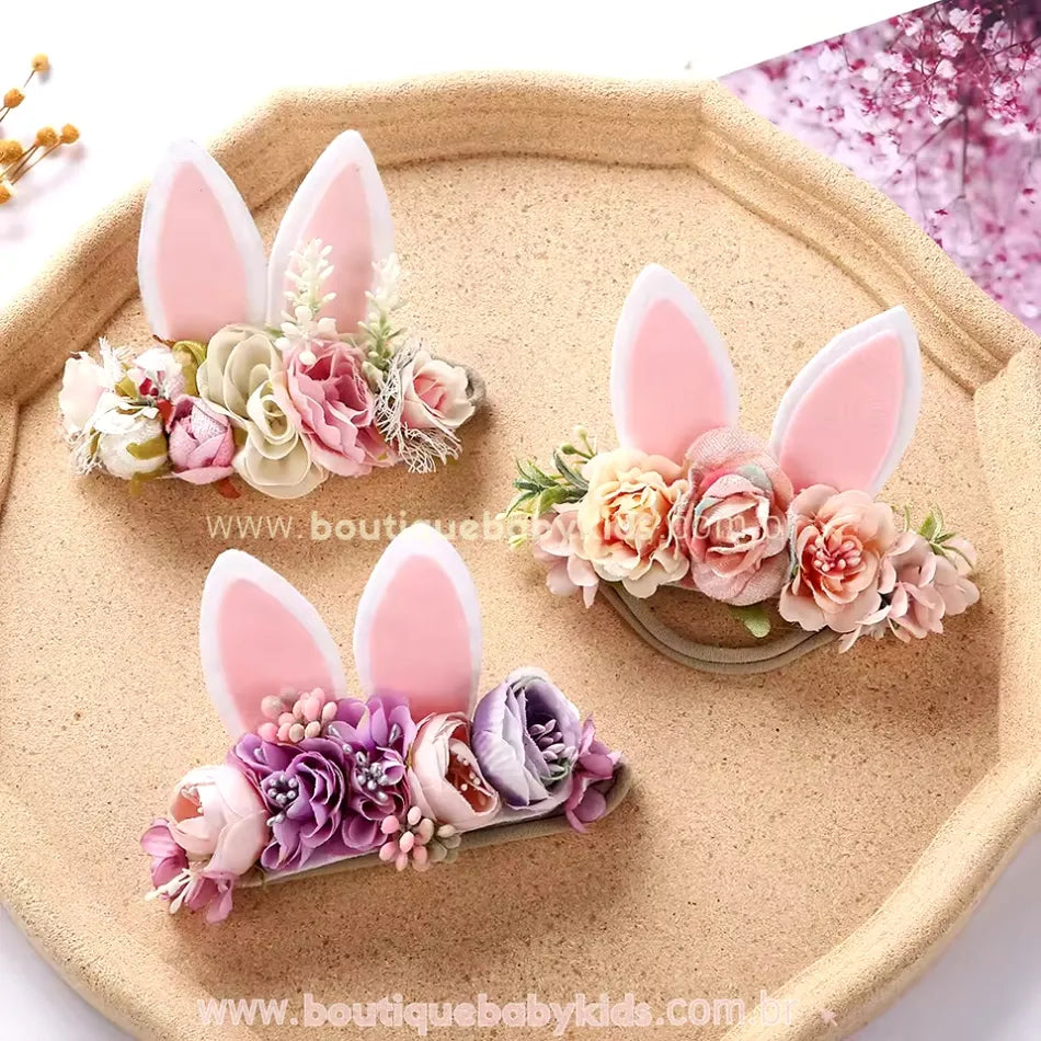 Trio de faixas de coelhinho expostas em um tabuleiro, mostrando a diversidade de cores e estilos disponíveis para complementar looks festivos.