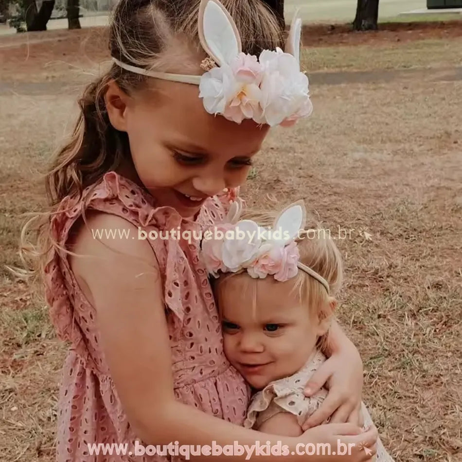 Duas irmãs usando a Faixa Temática Páscoa Jardim da Coelhinha em um momento especial ao ar livre, evidenciando a delicadeza e charme do acessório.