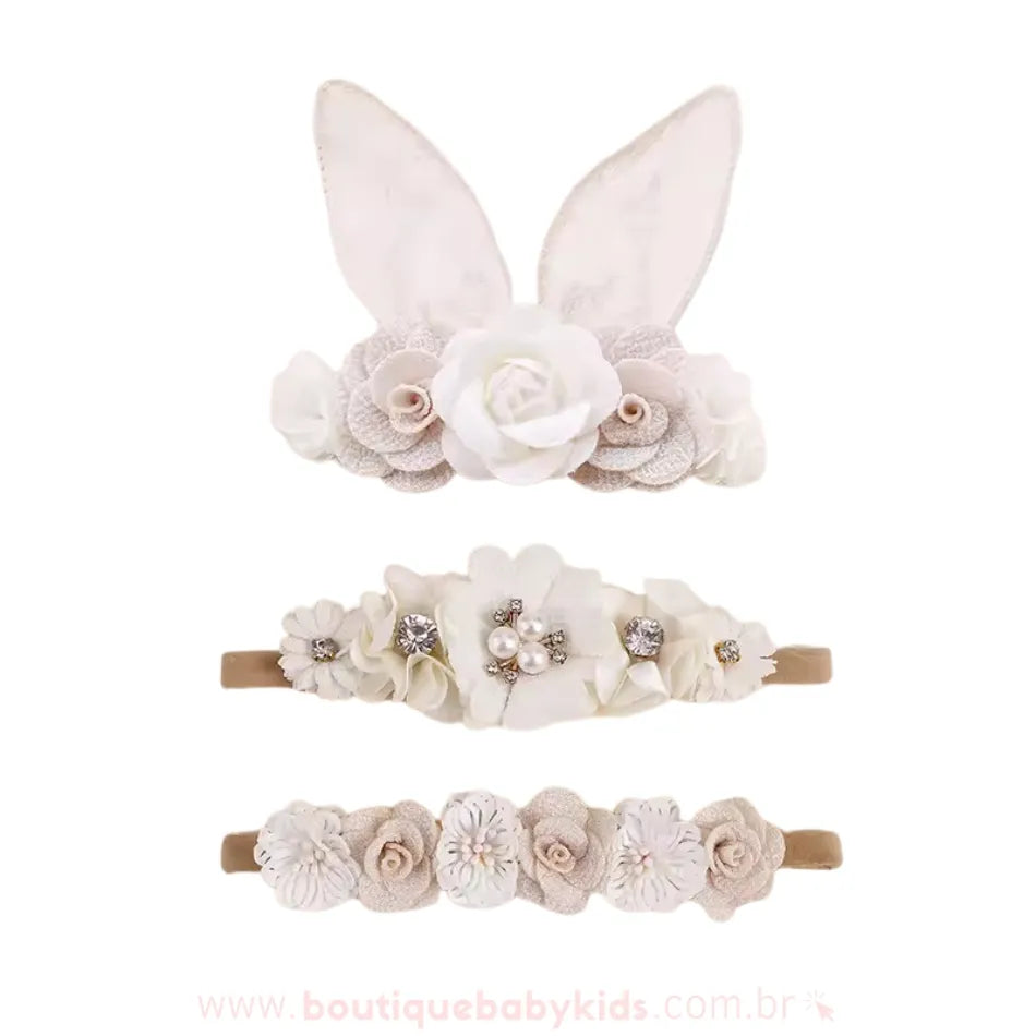 Conjunto de faixas florais em tons claros e sofisticados, com uma faixa de orelhinhas de coelho em tecido transparente e flores bege, uma faixa com detalhes brilhantes e pérolas e outra faixa decorada com pequenas flores rendadas.