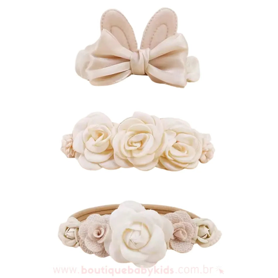 Kit com três faixas florais em tom bege, incluindo uma faixa com orelhinhas de coelho e laço de cetim perolado, uma faixa com flores grandes de cetim branco e outra com flores menores em um arranjo delicado.