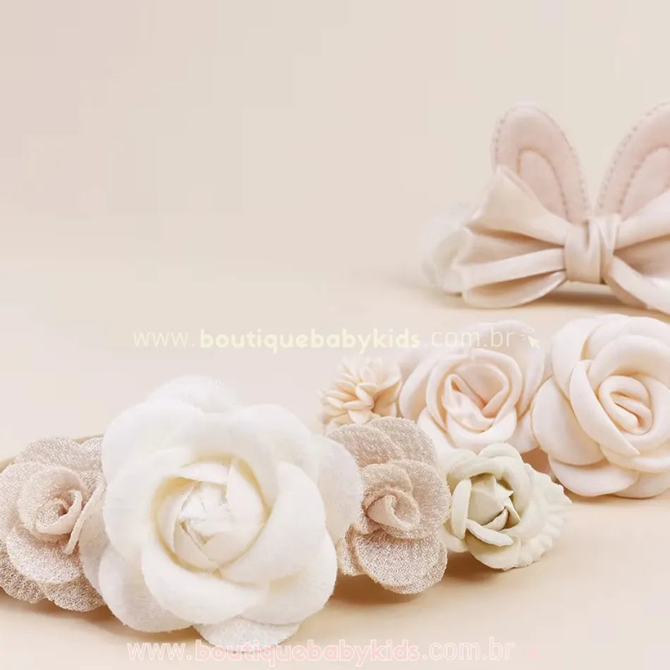 Close-up de faixas florais em tons neutros, destacando uma faixa bege com rosas brancas e bege e, ao fundo, uma faixa com orelhinhas de coelhinho e laço acetinado.