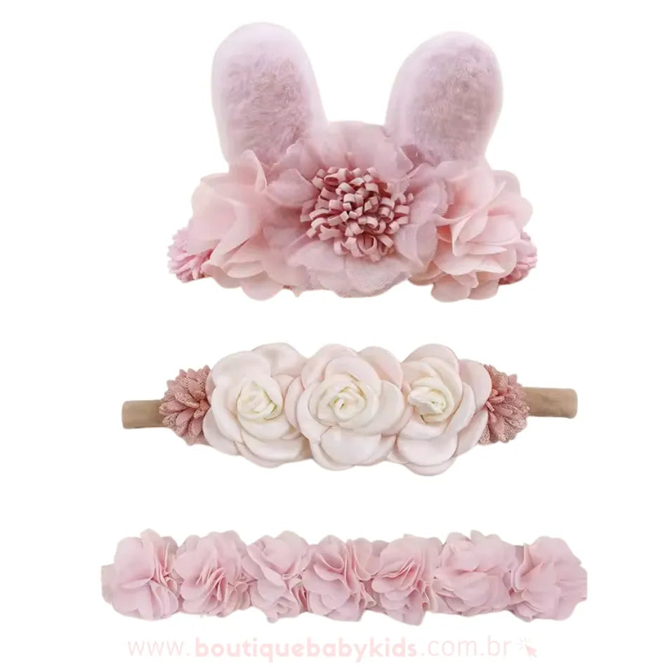 Conjunto de três faixas florais em tons de rosa, destacando uma faixa com orelhinhas de coelho peluciadas e flores volumosas, uma faixa com flores grandes de cetim e outra faixa decorada com camadas de pétalas delicadas.