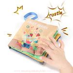 Mão infantil tocando um dos livros sensoriais, ativando um efeito sonoro ao virar a página. Ilustração mostra frutas como laranja e melancia.