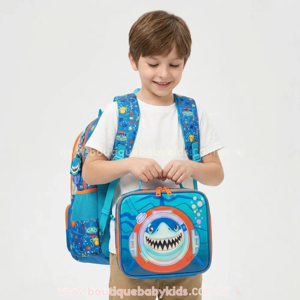 Criança segurando a lancheira escolar do kit Tubarão Aventureiro, destacando o desenho divertido de tubarão na frente.