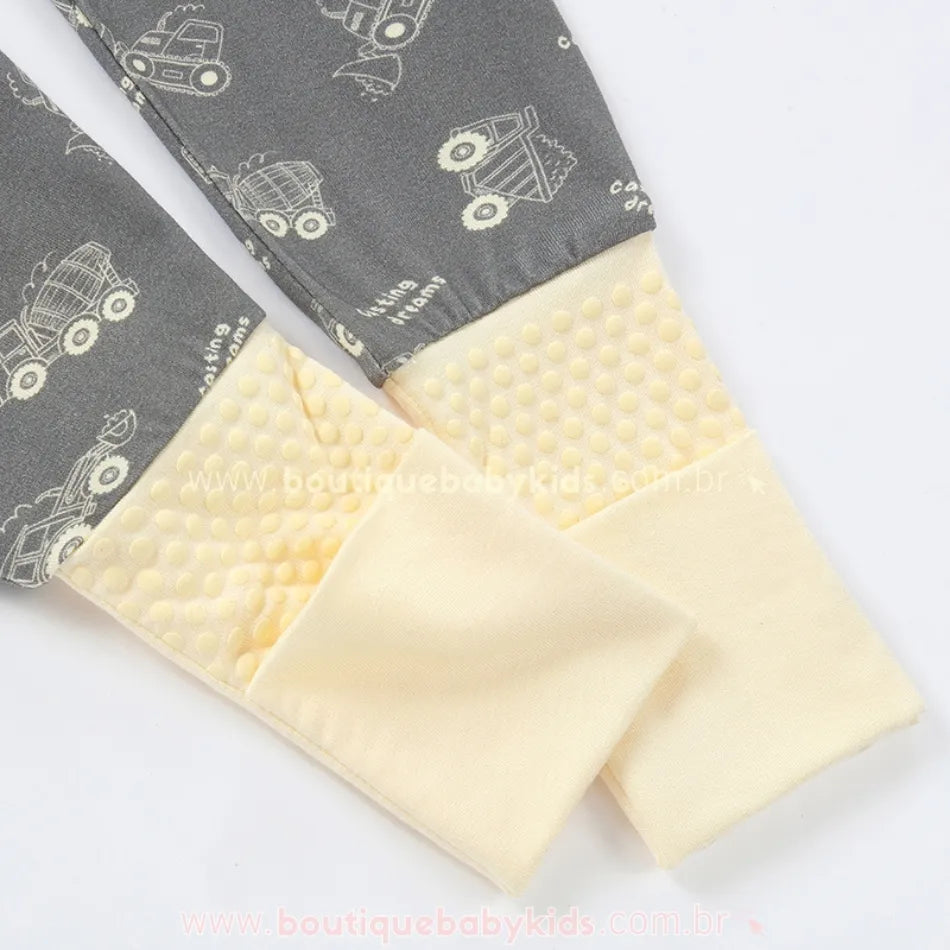 Detalhe do pezinho antiderrapante amarelo com punho dobrável do macacão cinza com estampa de tratores.