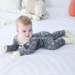 Bebê deitado com brinquedo ao fundo, usando o macacão com estampa de caminhões e tratores.