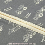 Close da estampa de veículos de construção no tecido cinza em fibra de bambu e zíper central do macacão.