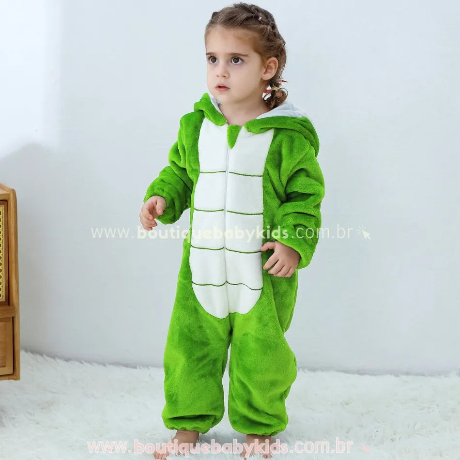 Criança em pé vestindo macacão de pelúcia verde com capuz de serpente e barriga branca. 