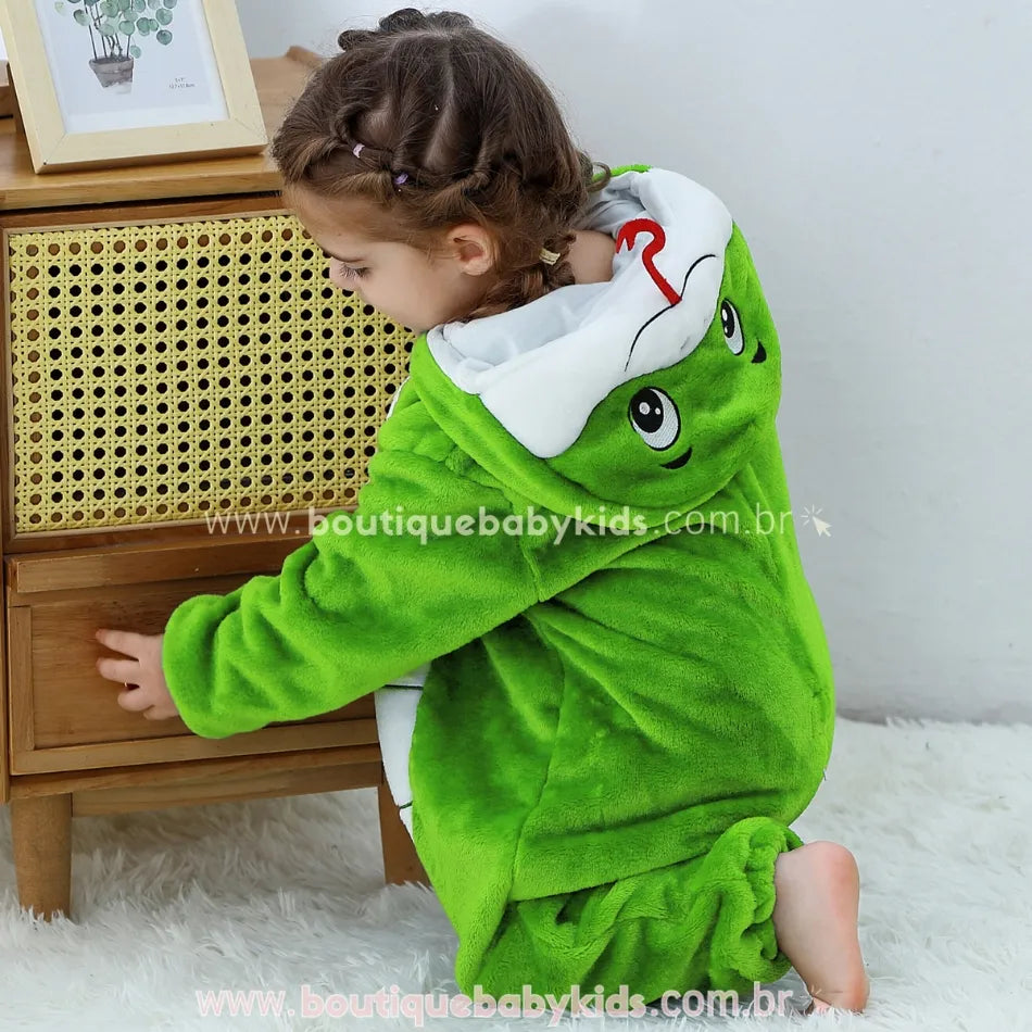 Criança agachada de lado, exibindo o capuz com rosto de serpente bordado e expressão simpática. 