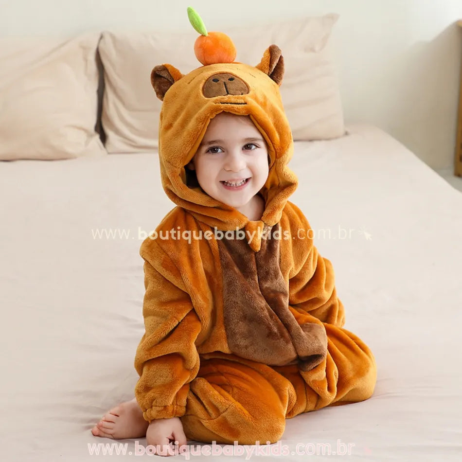 Criança sentada na cama com o capuz levantado, mostrando o rostinho feliz e o conforto do macacão.