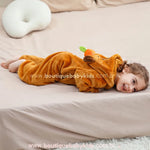 Criança deitada de lado sobre a cama, exibindo a parte de trás do capuz com orelhinhas e laranjinha.