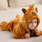 Criança deitada de bruços, com o rosto apoiado nas mãos e capuz da capivara com a laranjinha no topo em destaque.