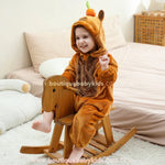 Criança brincando sentada em um cavalinho de madeira, vestindo o Macacão Capivara do Cerrado e sorrindo.