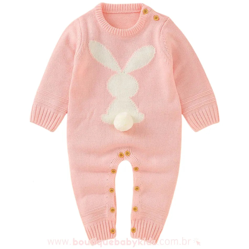 Macacão bebê tricot coelhinho na cor rosa, com coelho branco na parte frontal e rabinho pompom em destaque. Design de mangas longas e botões de madeira para fechamento. 