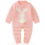 Macacão bebê tricot coelhinho na cor rosa, com coelho branco na parte frontal e rabinho pompom em destaque. Design de mangas longas e botões de madeira para fechamento. 