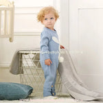 Bebê posando ao lado de um cesto, usando o Macacão Bebê Tricot Coelhinho azul. O fechamento entre as pernas por botões facilita a troca de fraldas. 