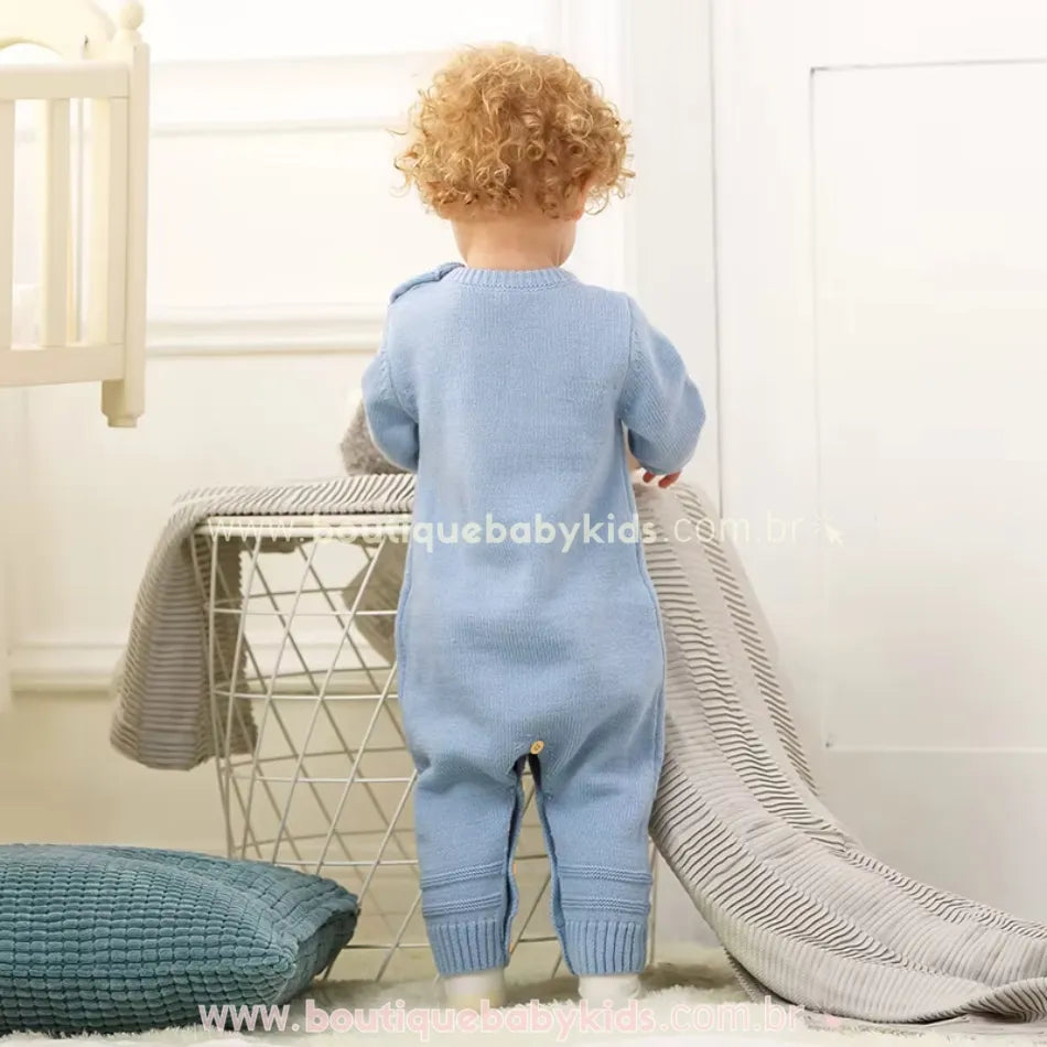 Vista traseira do bebê vestindo o macacão azul. O modelo é liso na parte de trás, com punhos ajustados e tecido tricotado. 