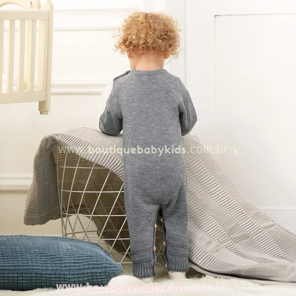 Visão traseira do bebê vestindo o macacão tricot cinza. O modelo tem acabamento liso na parte de trás e detalhes canelados nos punhos e tornozelos. 