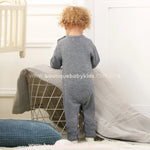 Visão traseira do bebê vestindo o macacão tricot cinza. O modelo tem acabamento liso na parte de trás e detalhes canelados nos punhos e tornozelos. 