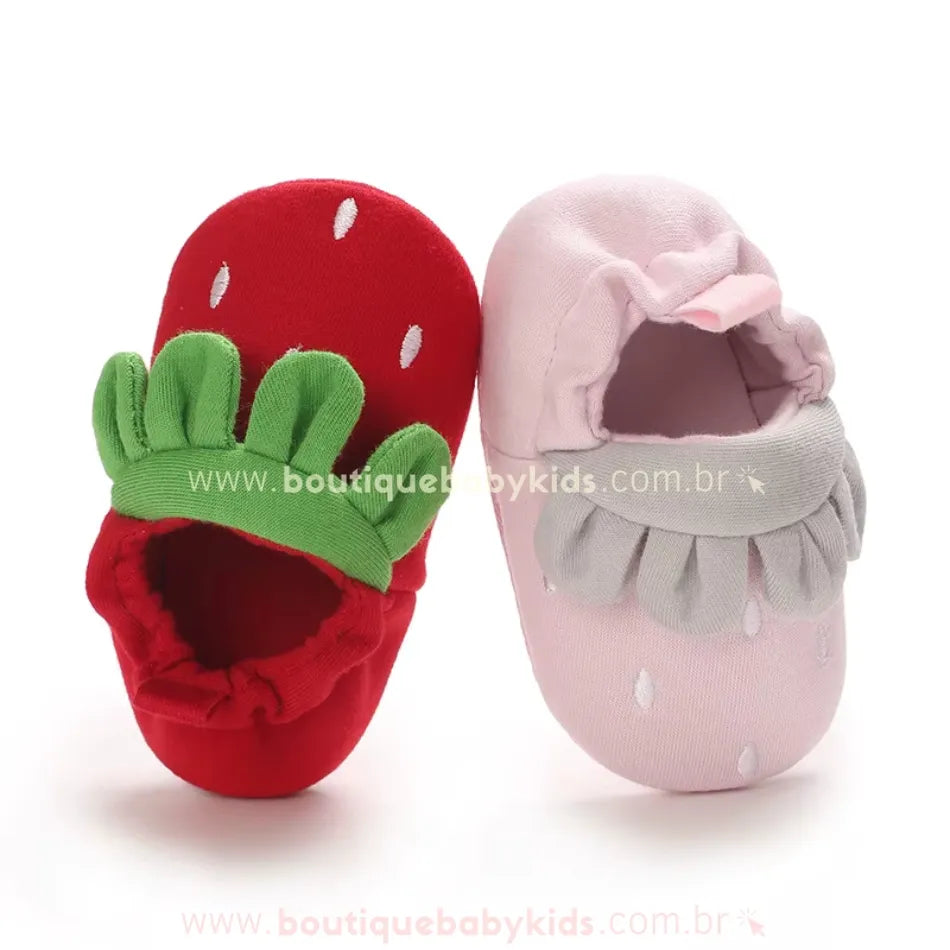 Pantufinhas de bebê nas cores vermelha e rosa, exibindo um design inspirado em morangos com acabamento macio e elástico confortável na abertura.