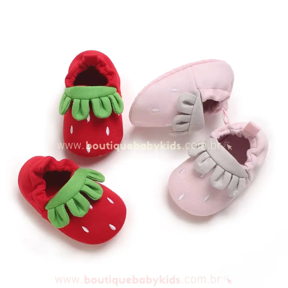 Duas opções de pantufinha de bebê moranguinho: uma na cor vermelha com detalhe verde e outra rosa com detalhe cinza, ambas com formato fofo de morango.