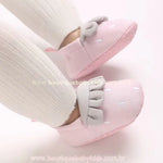 Pantufinha de bebê rosa vestida nos pezinhos de um bebê com meias brancas, mostrando o ajuste confortável e o design fofo do modelo. 