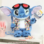 Pelúcia Stitch 30 cm estilo havaiano com camisa floral, colar dourado e óculos vermelhos, exposta em ambiente decorado.