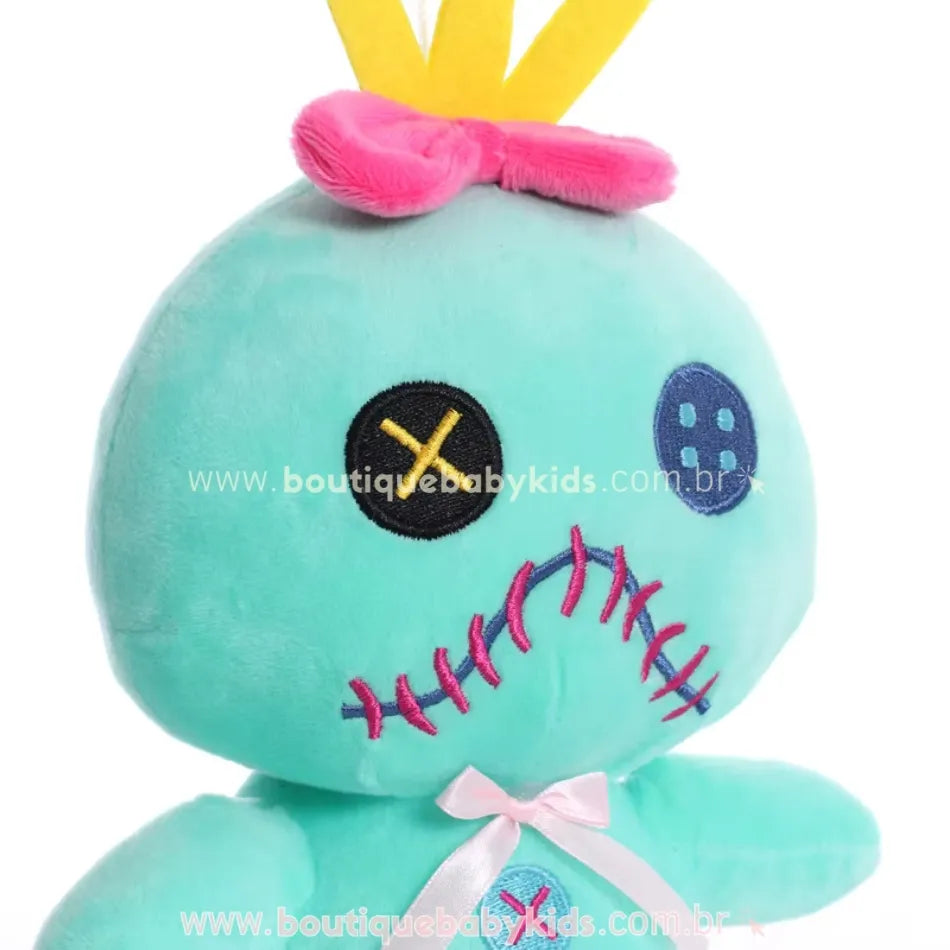 Close da pelúcia Scrump com olhos de botão, boca costurada em rosa e coroa amarela com laço rosa.