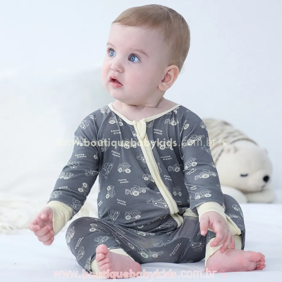 Bebê sentado usando macacão cinza com estampa de caminhõezinhos, feito em fibra de bambu, com punhos creme e zíper frontal – Boutique Baby Kids.