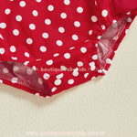 Detalhe da parte inferior do romper com estampa de poás brancos sobre fundo vermelho e fechamento por botões de pressão