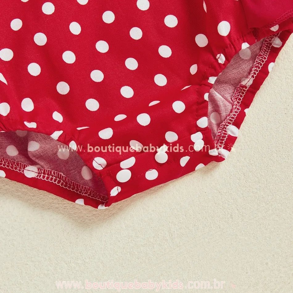 Detalhe da parte inferior do romper com estampa de poás brancos sobre fundo vermelho e fechamento por botões de pressão