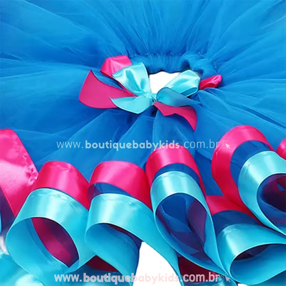 Vista superior da saia infantil inspirada na personagem Poppy, com camadas de tule azul e laço decorativo duplo em rosa e azul na cintura.
