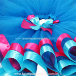 Vista superior da saia infantil inspirada na personagem Poppy, com camadas de tule azul e laço decorativo duplo em rosa e azul na cintura.